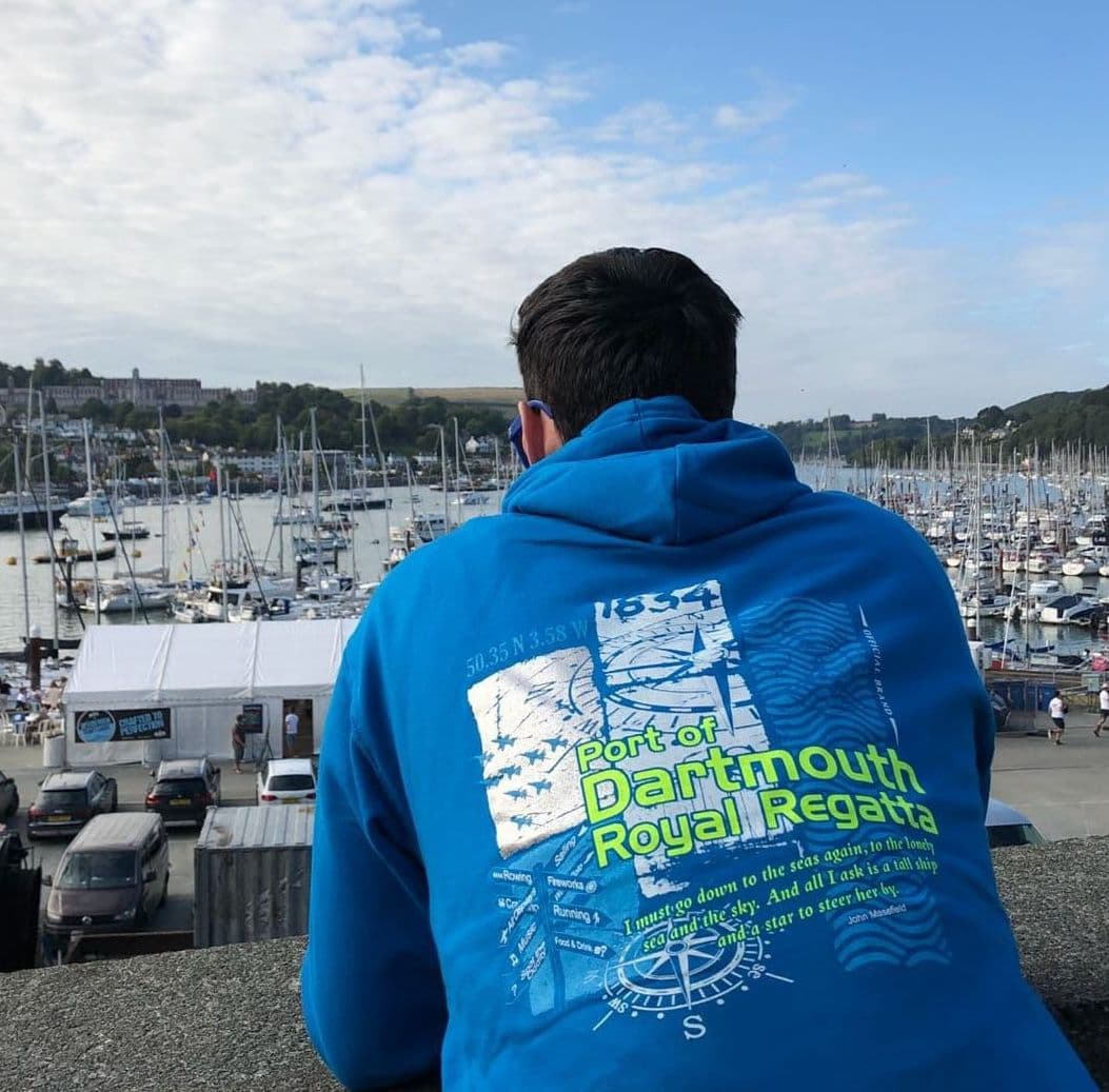 Person wearing a blue Port of Dartmouth Royal Regatta printed hoodie, overlooking the harbour and moored yachts