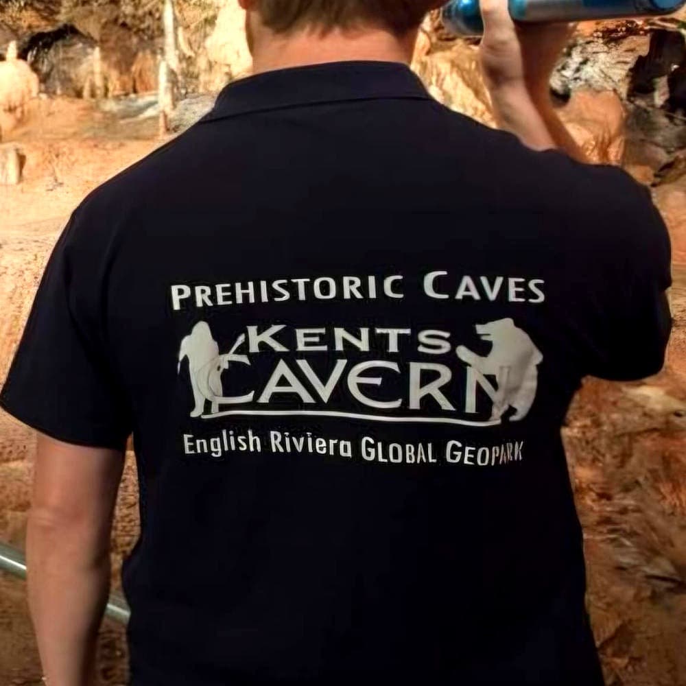 Black polo shirt screen-printed with the Kents Cavern Prehistoric Caves logo, worn inside the caves