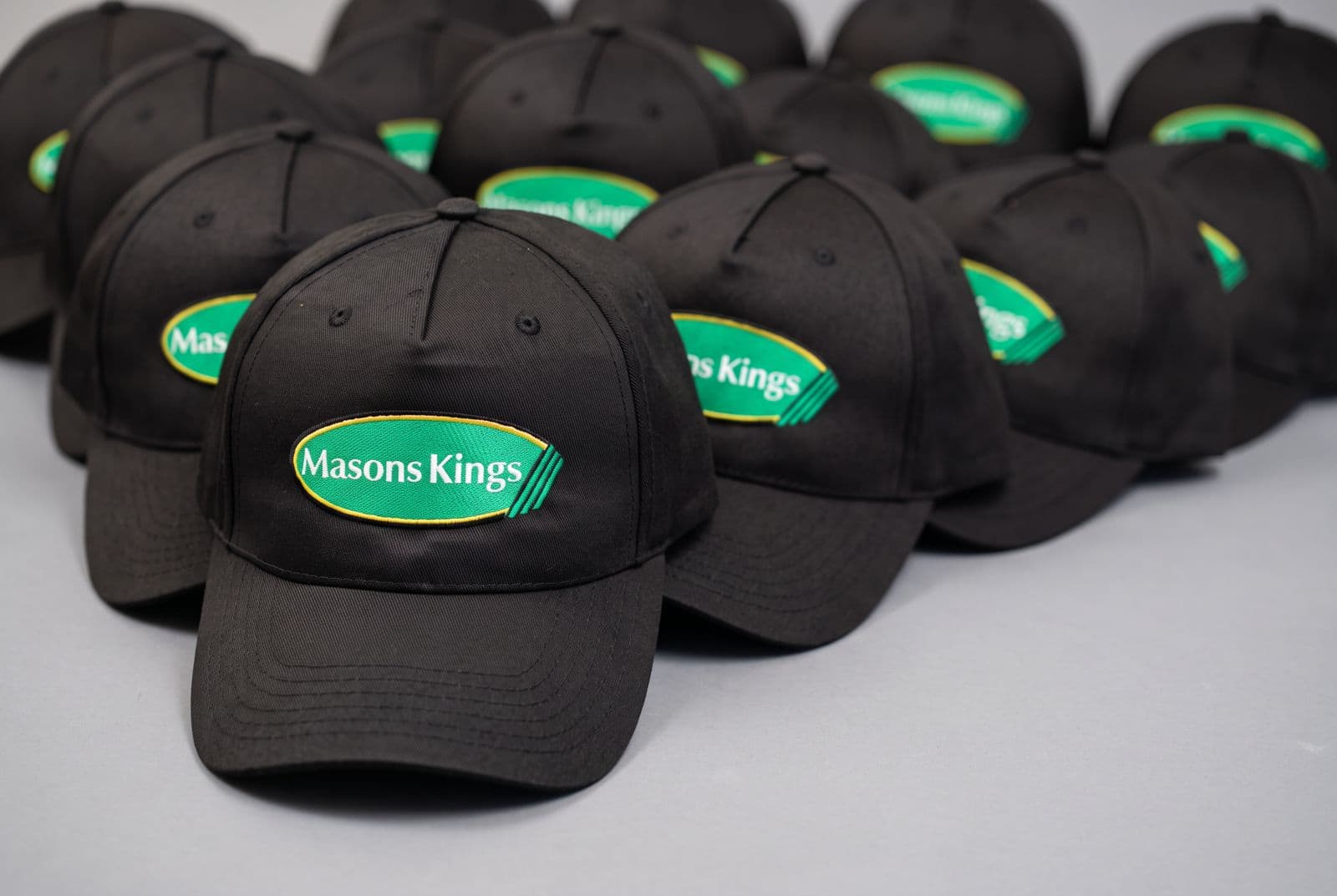 Rows of black baseball caps embroidered with the Masons Kings logo, ready for a bulk order