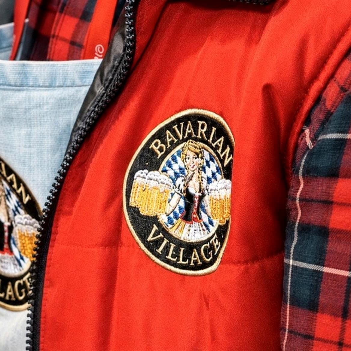 Red bodywarmer with an embroidered Bavarian Village badge, layered over tartan and denim shirts