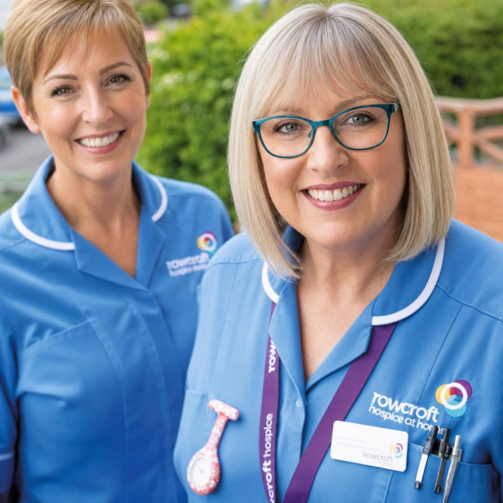 Two care staff wearing blue Rowcroft Hospice uniforms embroidered with the charity logo